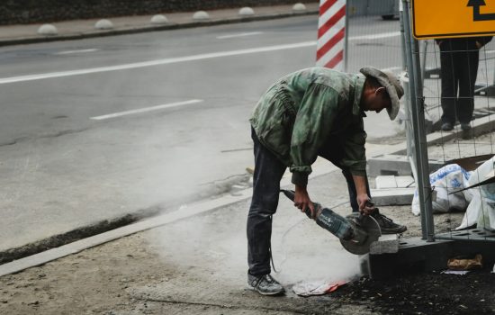 man in green jacket and blue denim jeans holding black and gray power tool